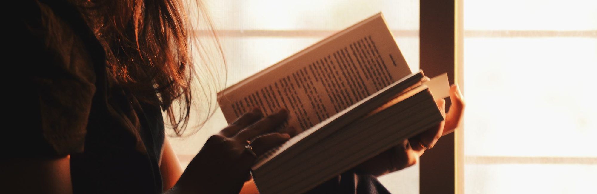 A woman sitting by a bright window reading a book