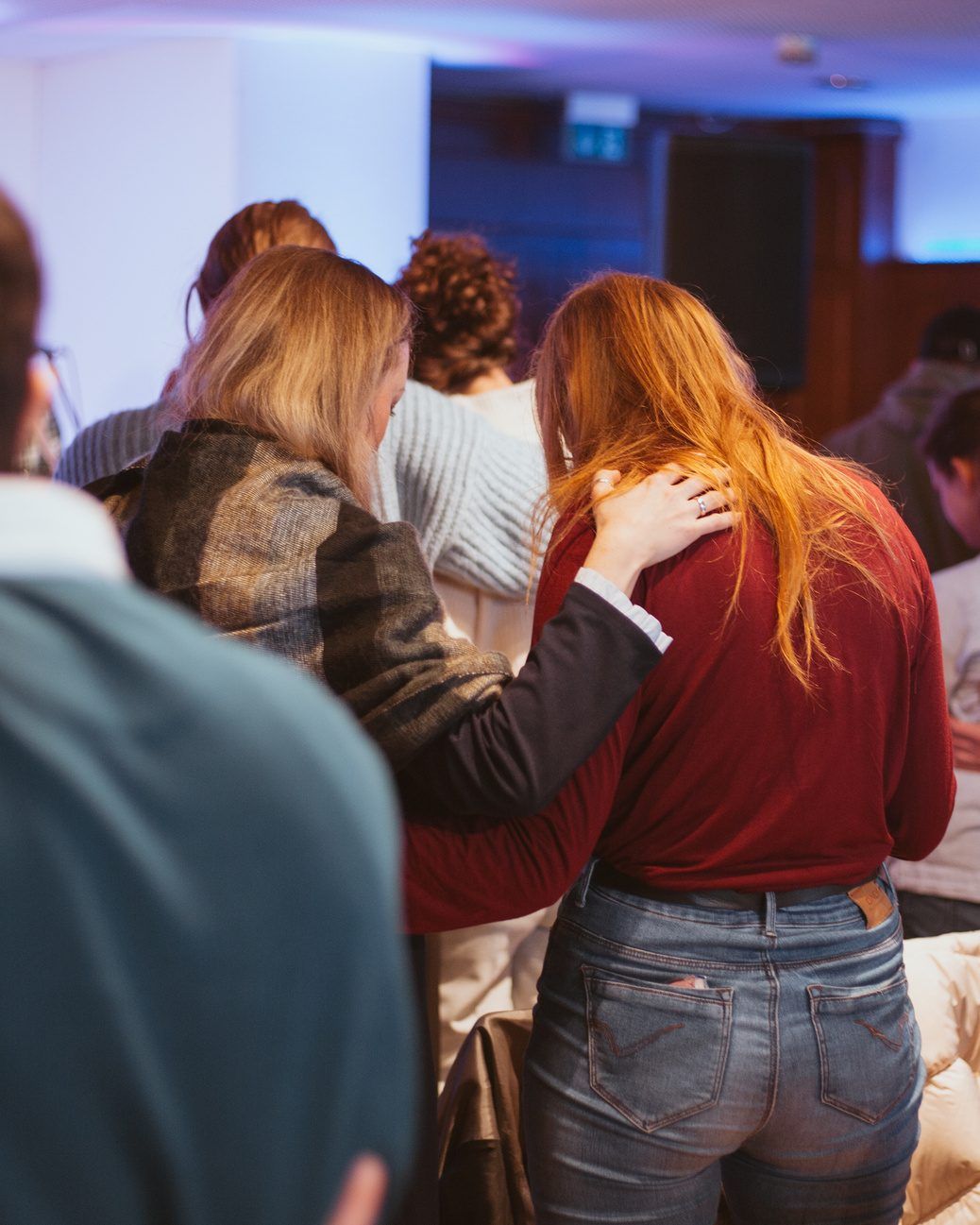 A woman praying with her hand on the shoulder of another woman in a red jumper