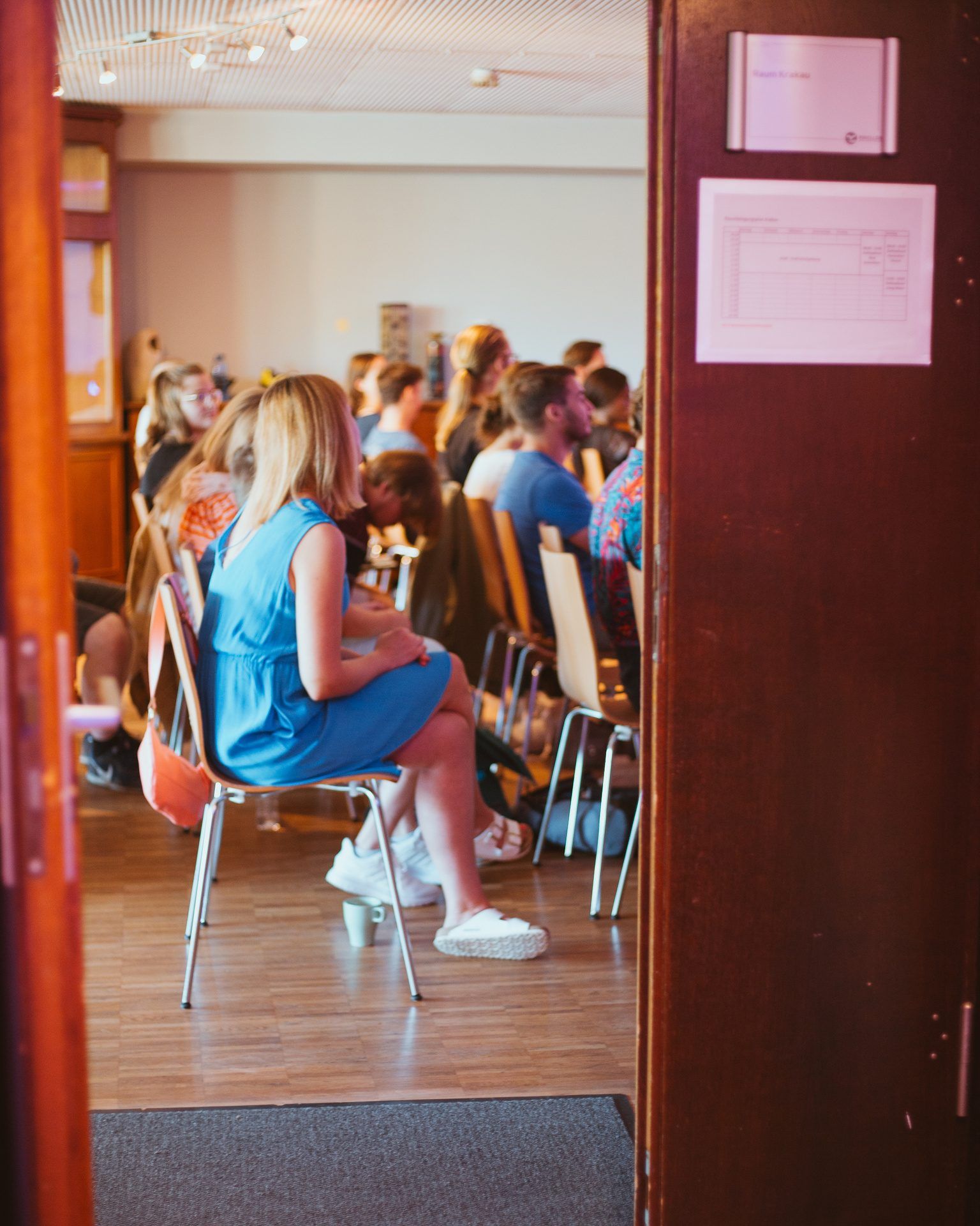 View through an open door into a room where people sit in rows of chairs