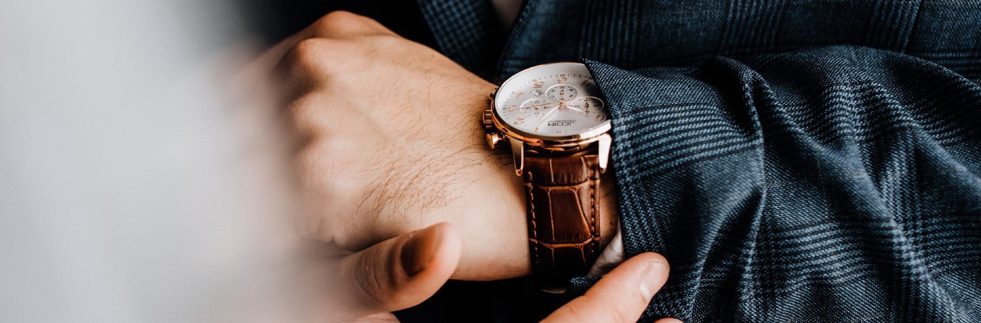 Hand adjusting a wristwatch with a leather strap on the wrist of a man in a jacket