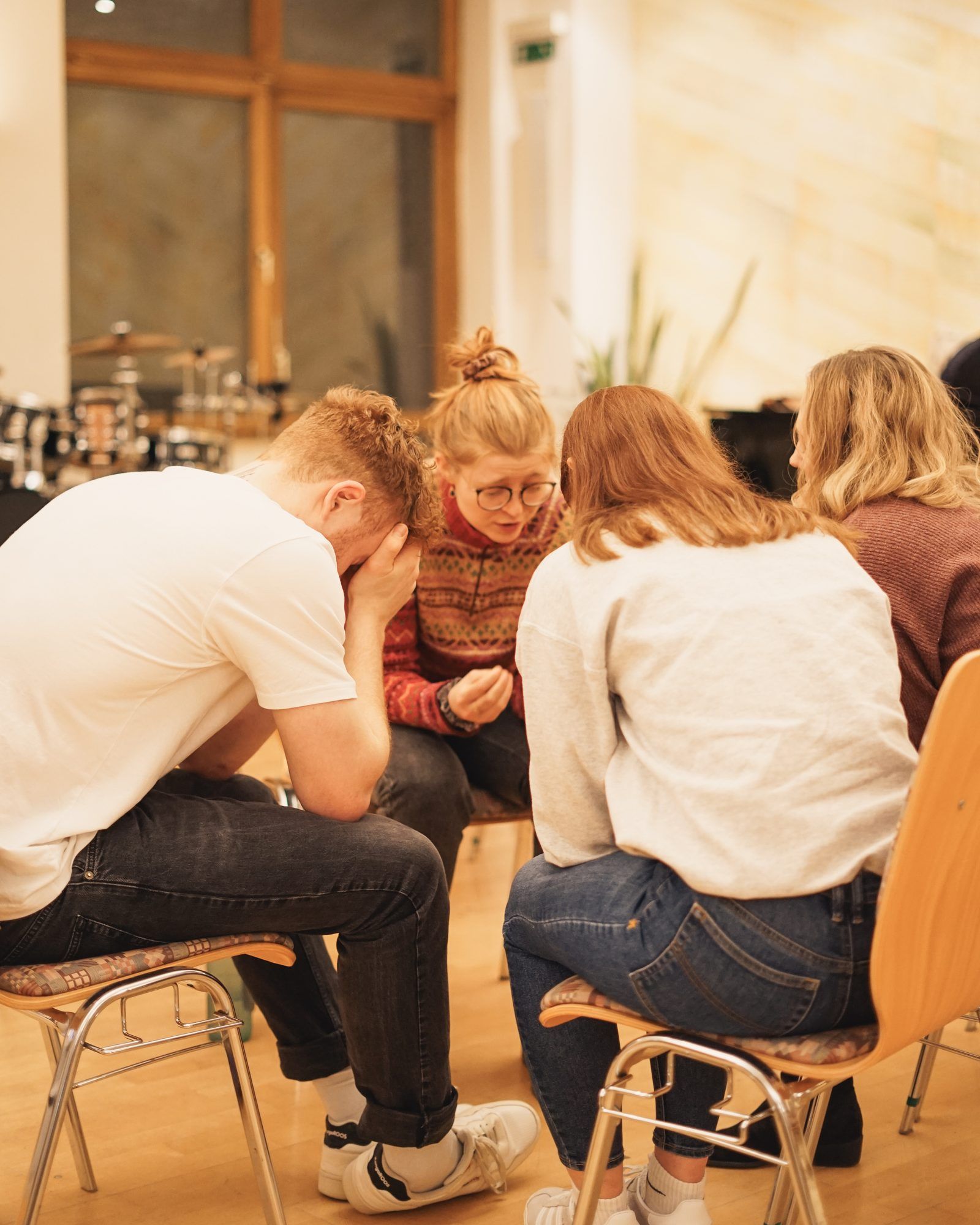 A small group sitting close together on chairs and praying, a young man with his face in his hands