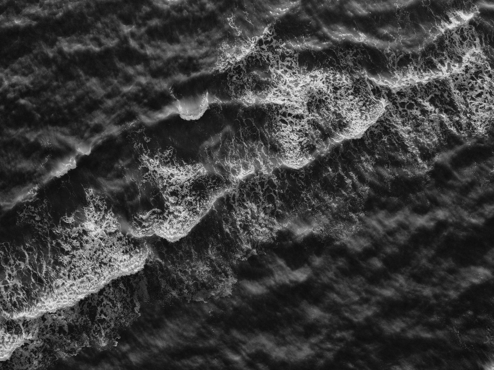 Ocean waves with white foam seen from above, in black and white