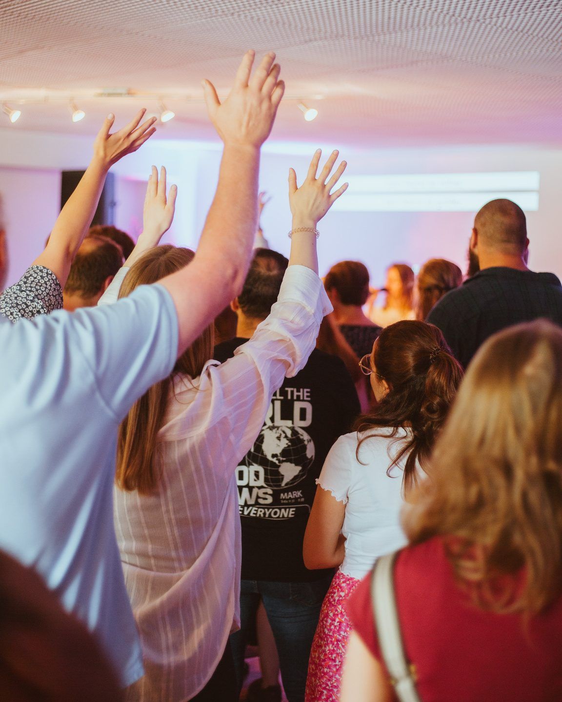 People at a church service raising their hands, with a singer on a stage in purple light at the front