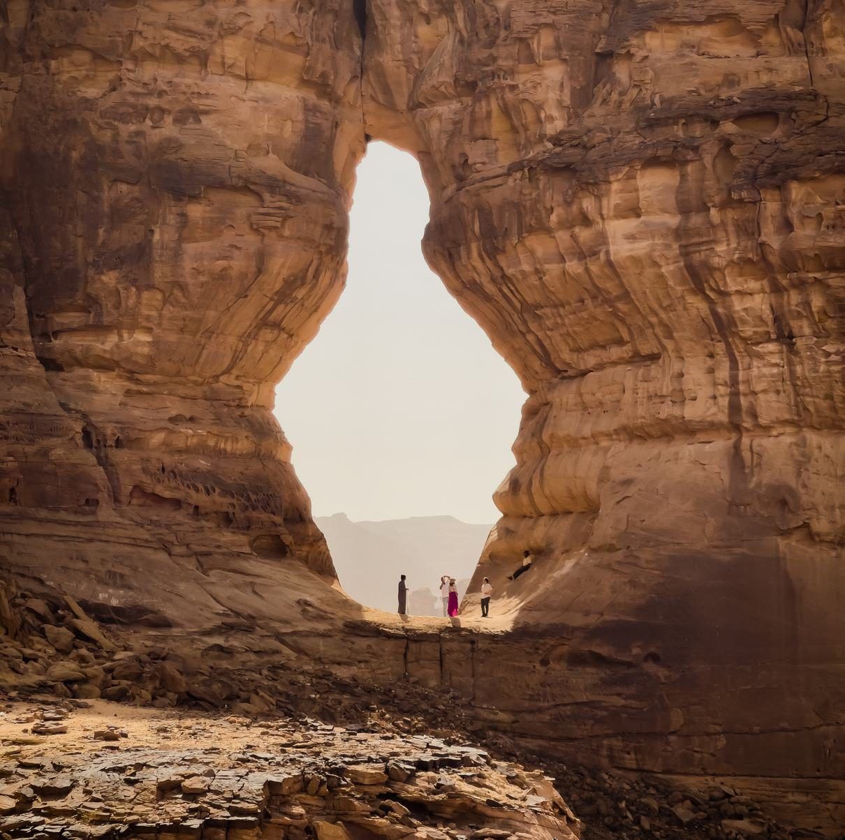 People standing in a teardrop-shaped rock arch in a sandstone desert landscape