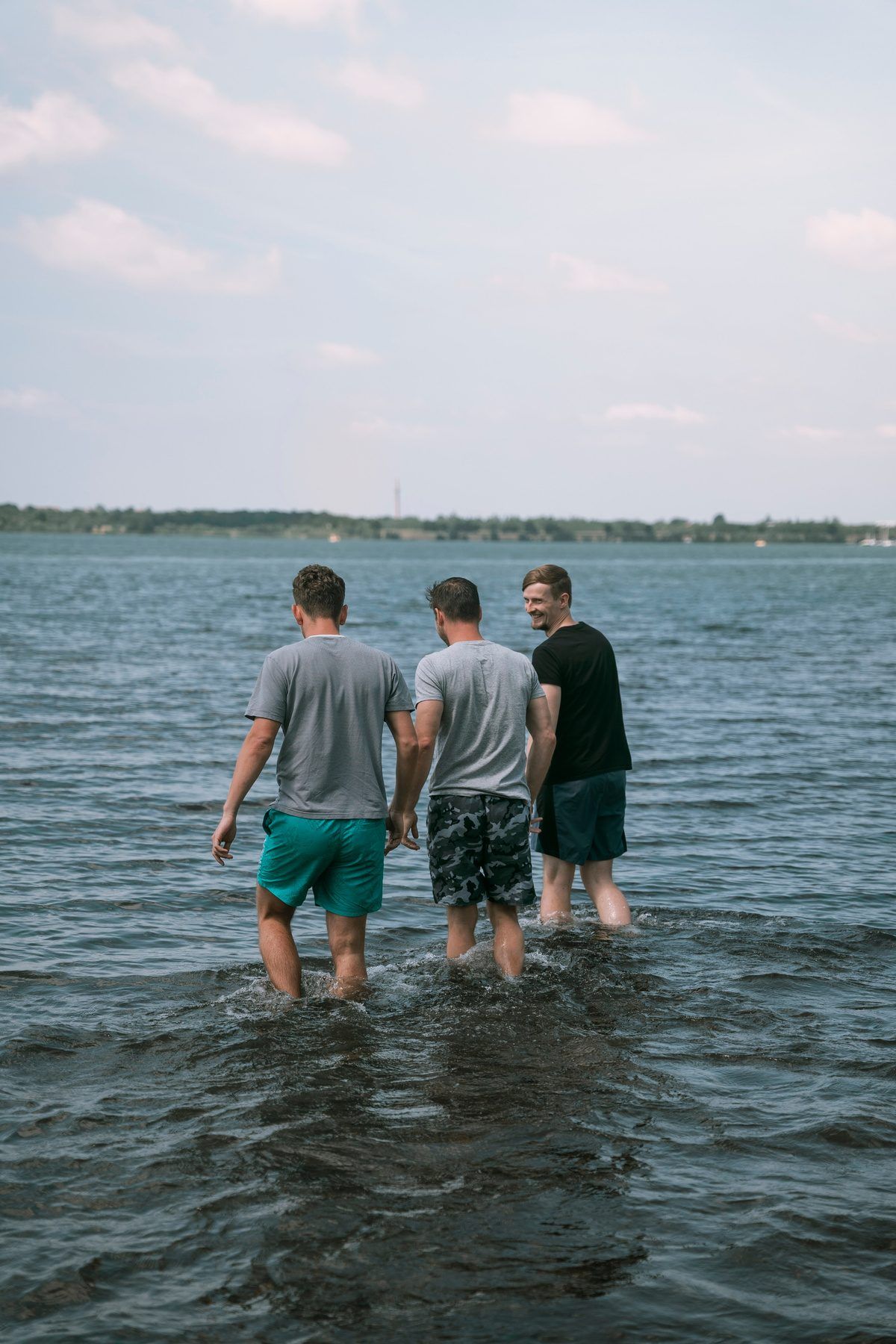 Three men wading into a lake, seen from behind
