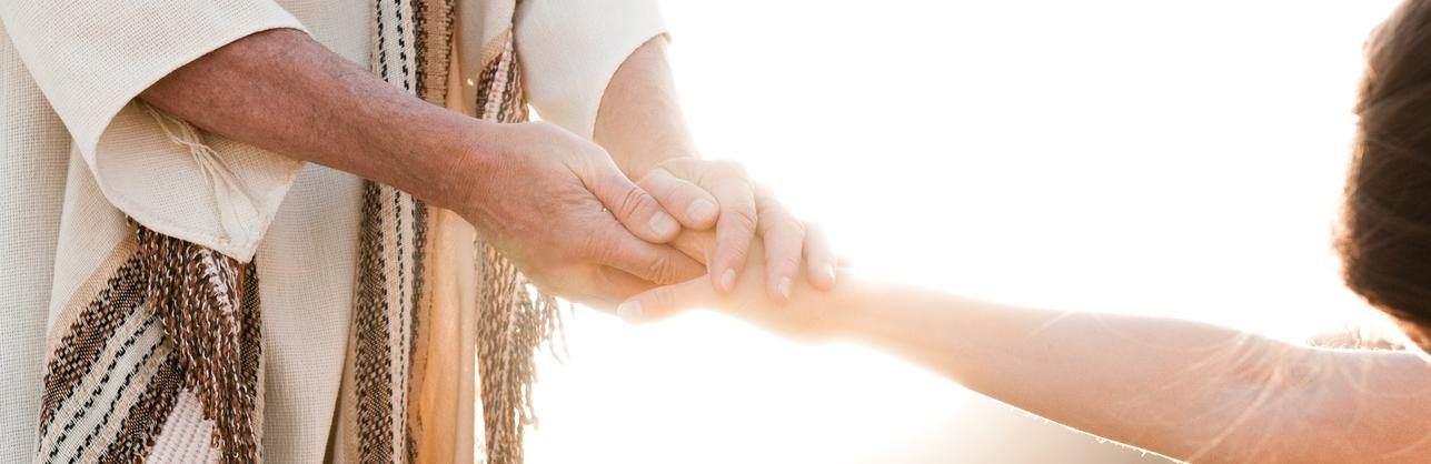 A hand in a striped robe taking hold of an outstretched hand in bright backlight