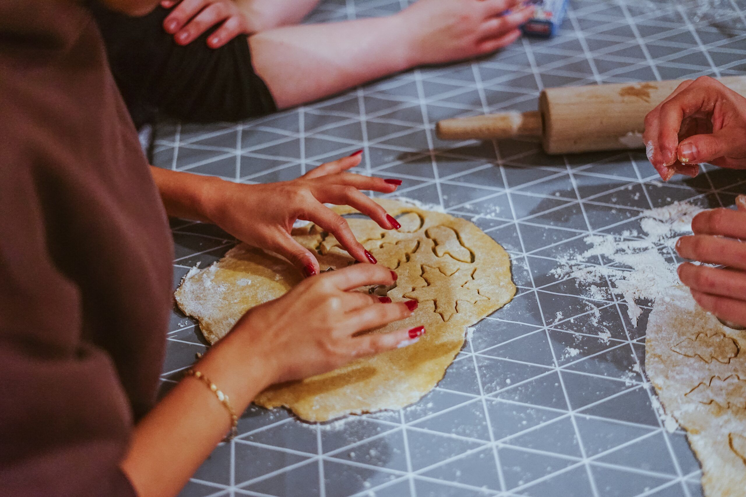 Several pairs of hands rolling out and cutting biscuit dough together