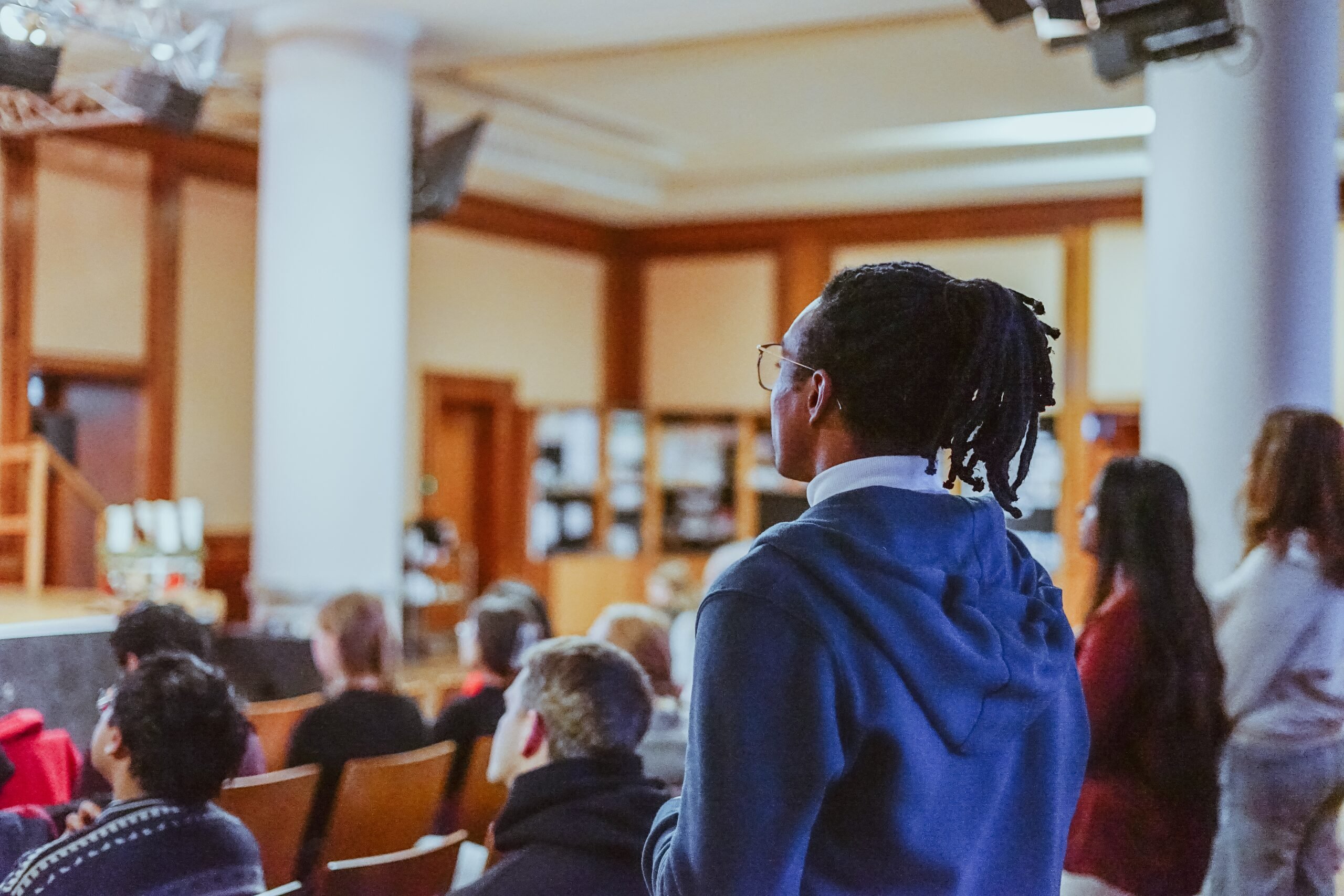 A young man in a blue hoodie listening during the service, surrounded by the congregation