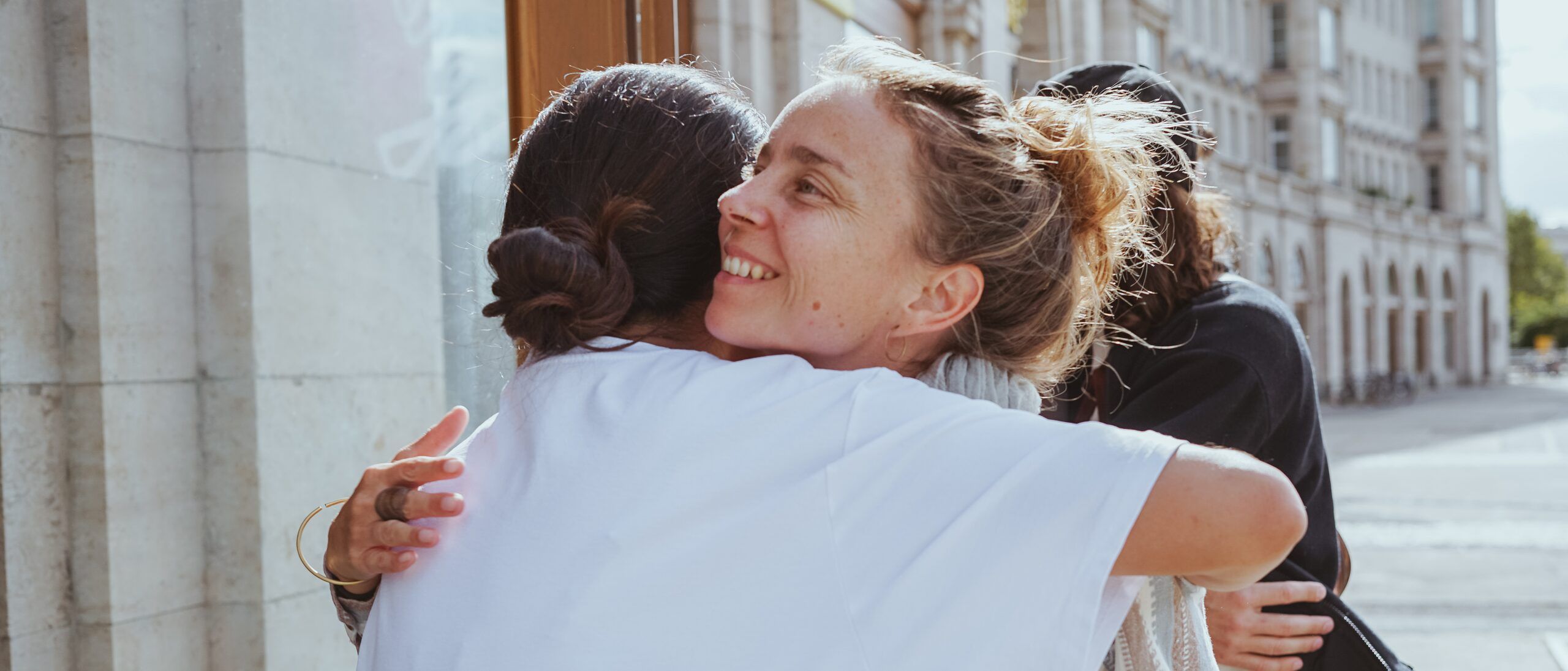 People greeting and hugging each other in front of the entrance on a sunny day, a small boy among them